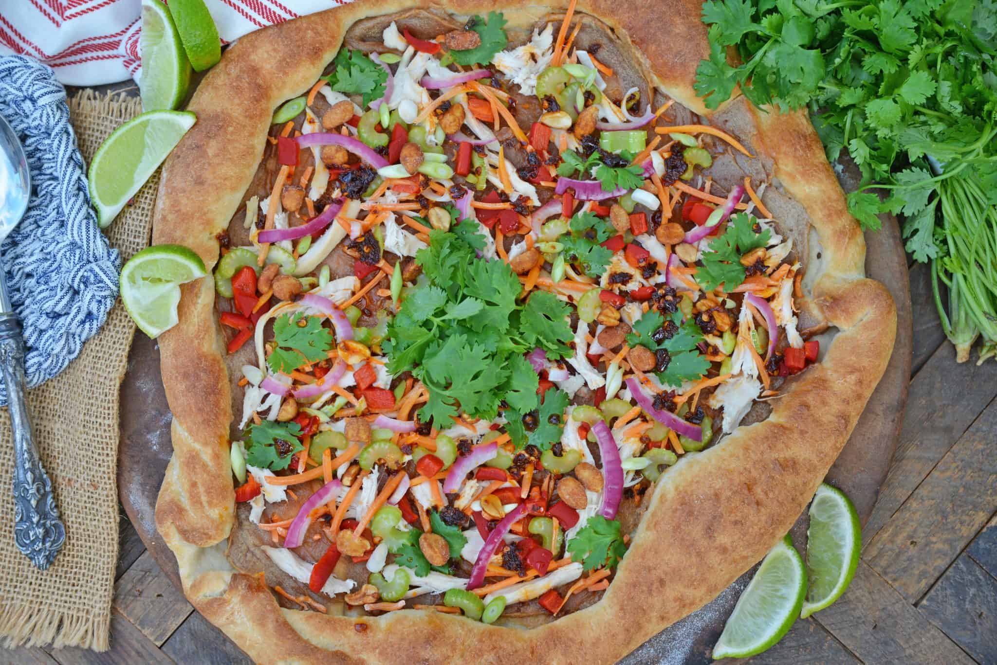 Spicy Thai Chicken Pizza uses a rich peanut satay sauce with shredded chicken, colorful vegetables and topped with sweet honey roasted peanuts and spicy chili oil. #thaichicken #homemadepizza www.savoryexperiments.com 