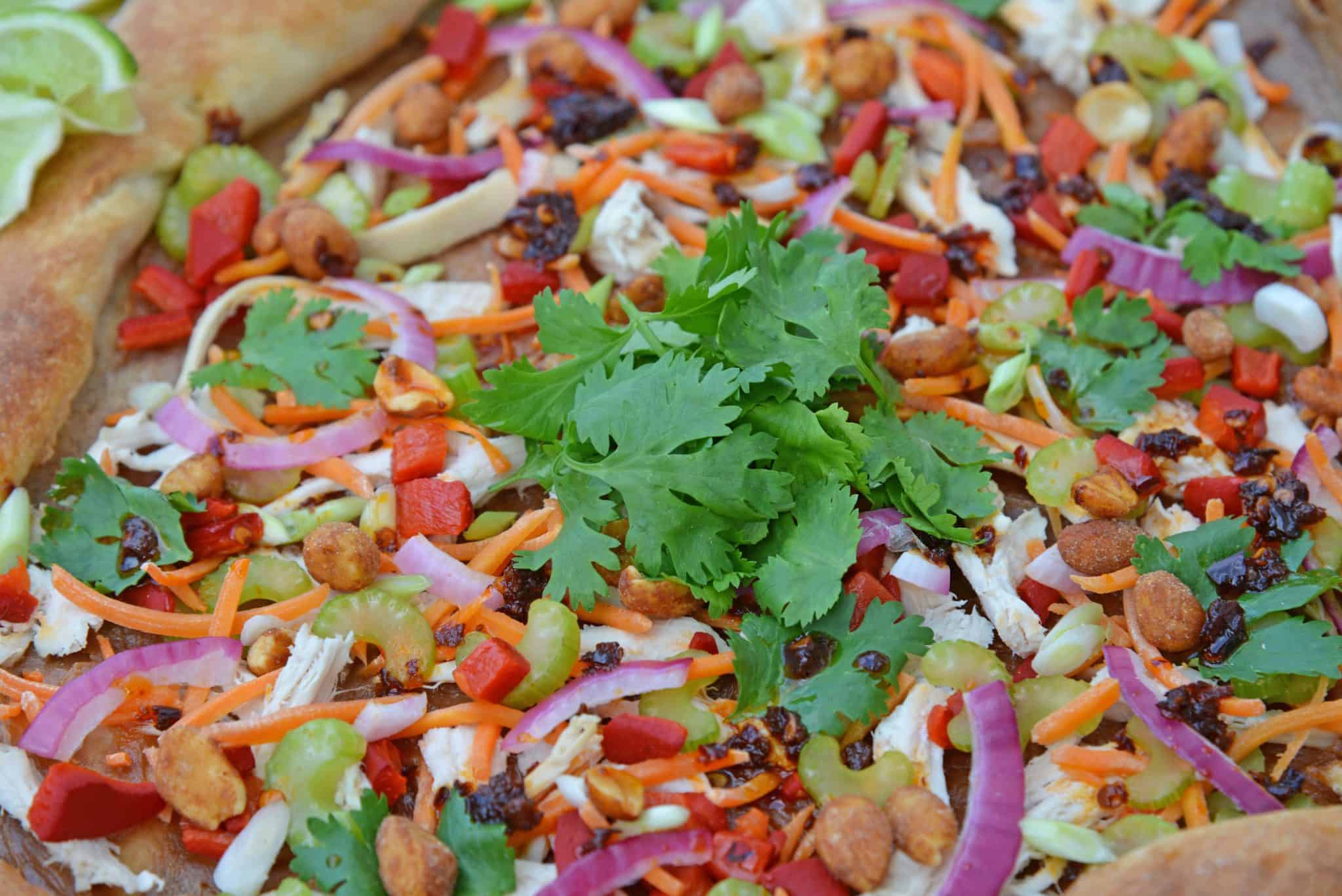 Spicy Thai Chicken Pizza uses a rich peanut satay sauce with shredded chicken, colorful vegetables and topped with sweet honey roasted peanuts and spicy chili oil. #thaichicken #homemadepizza www.savoryexperiments.com 