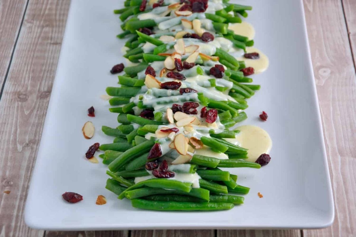 Thanksgiving sides green beans covered in cream sauce on a white plate with cranberries