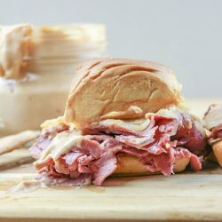 Corned beef slider sandwich recipes on a cutting board with sauce in the background