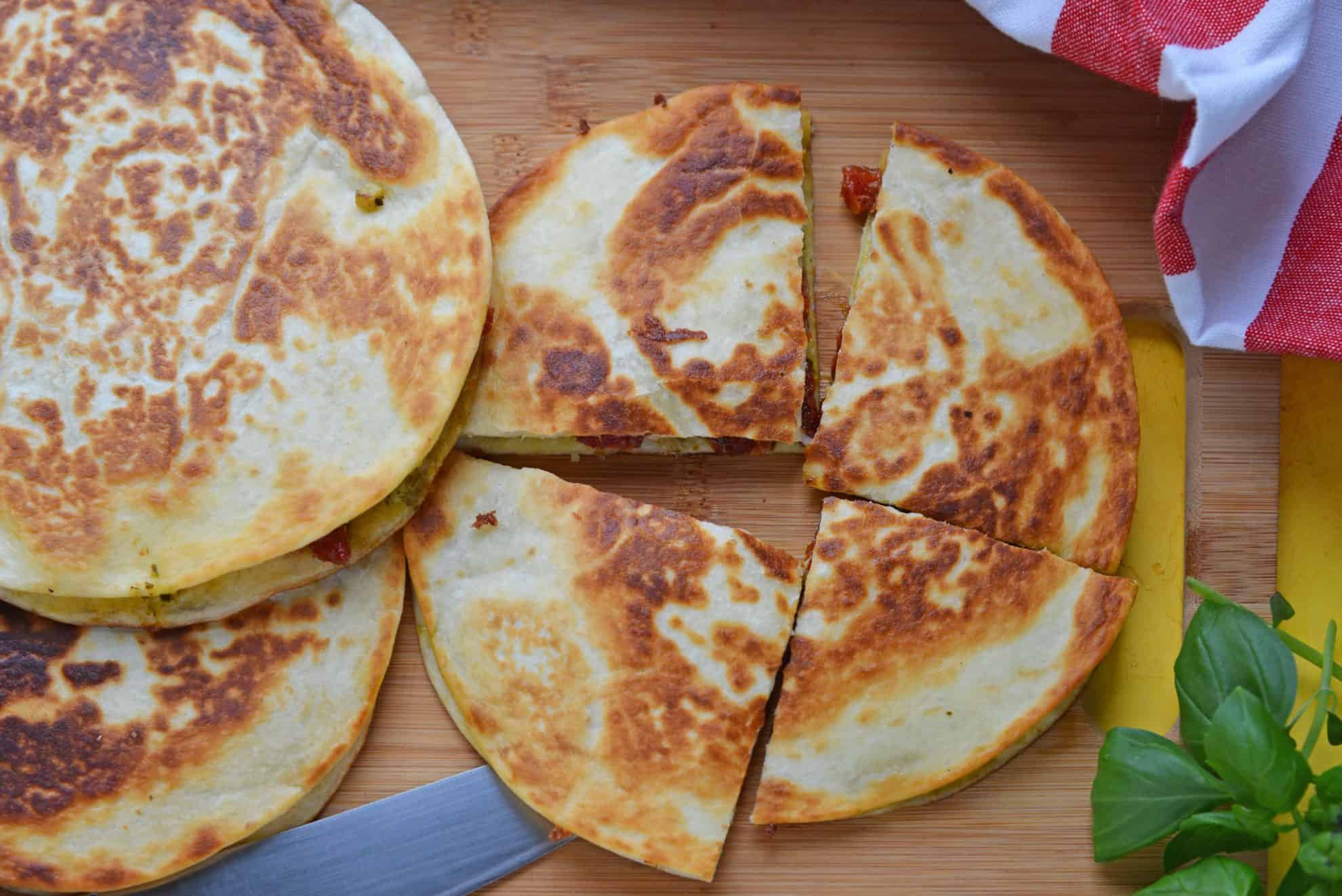 Caprese Quesadillas combine homemade pesto sauce with sun dried tomatoes and gooey mozzarella cheese. Serve for lunch, dinner or even as a party appetizer! #quesadillarecipe #capresequesadilla www.savoryexperiments.com 