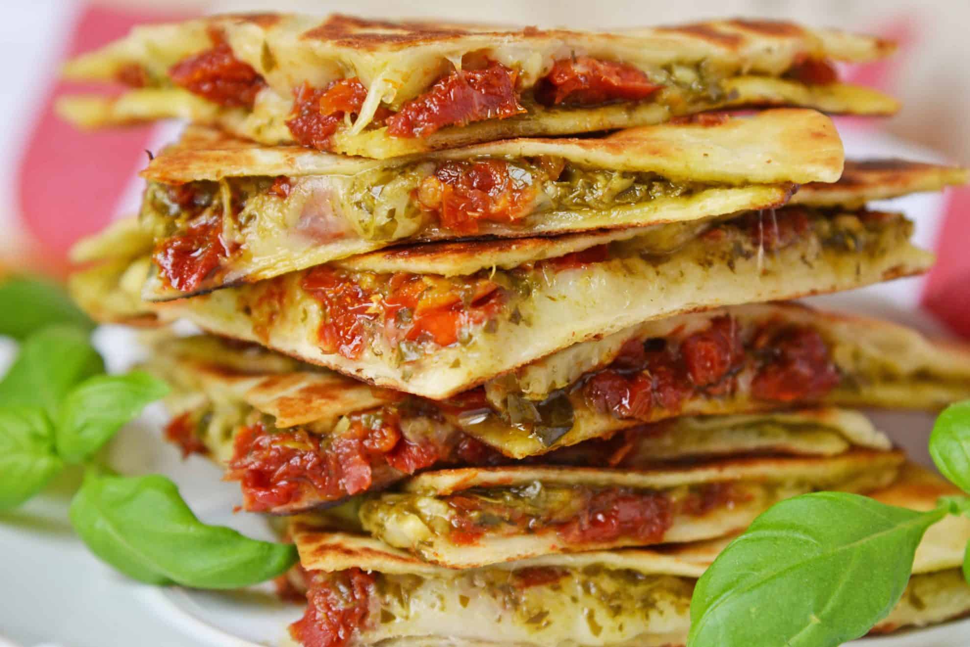 Caprese Quesadillas combine homemade pesto sauce with sun dried tomatoes and gooey mozzarella cheese. Serve for lunch, dinner or even as a party appetizer! #quesadillarecipe #capresequesadilla www.savoryexperiments.com 