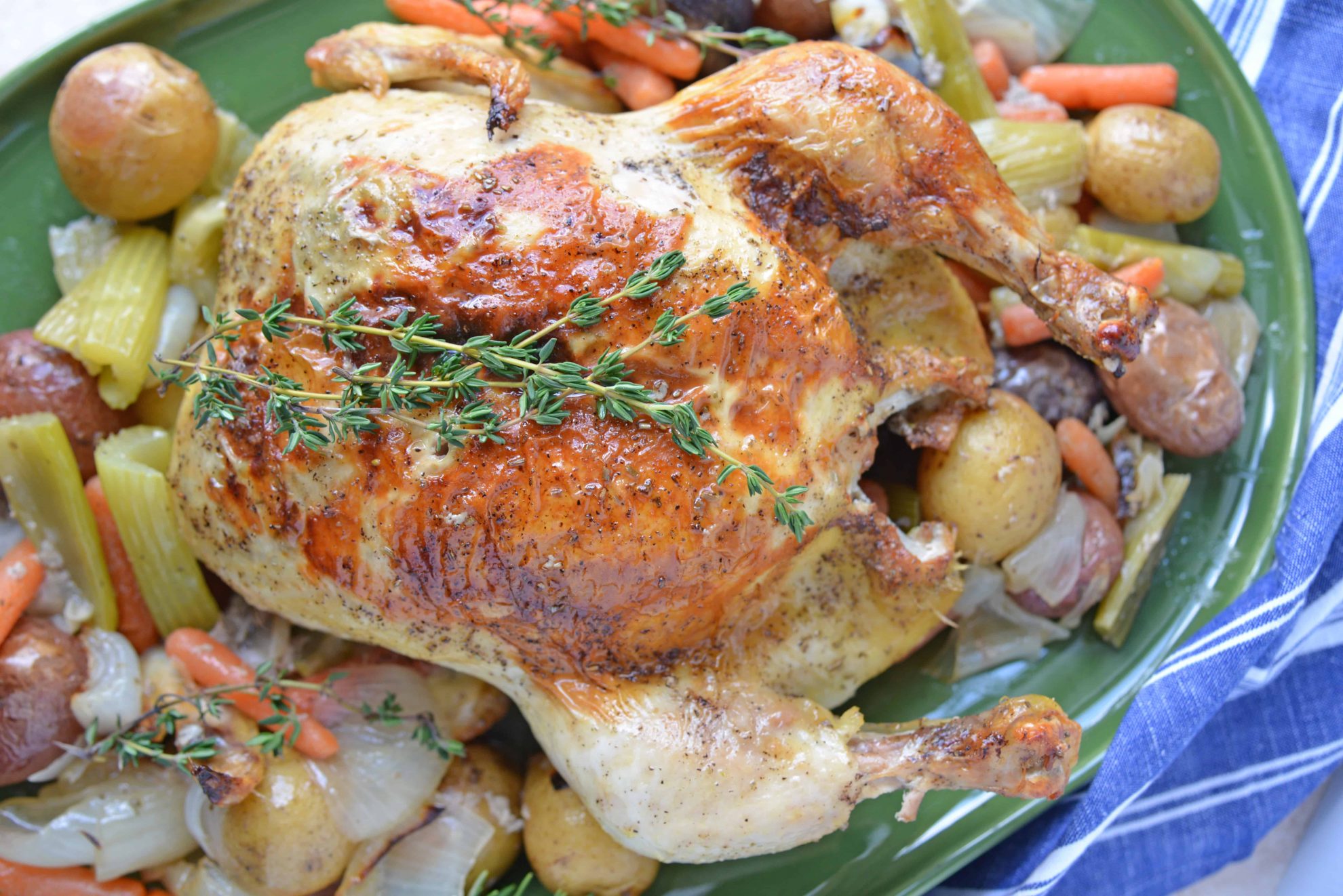 Overhead of roast chicken on a green platter surrounded by vegetables