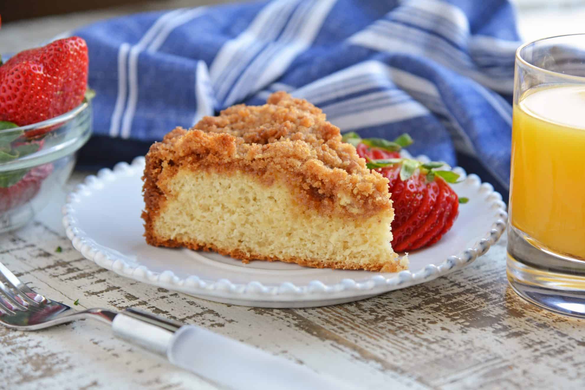 Slice of coffee cake on a white plate with sliced strawberries. 