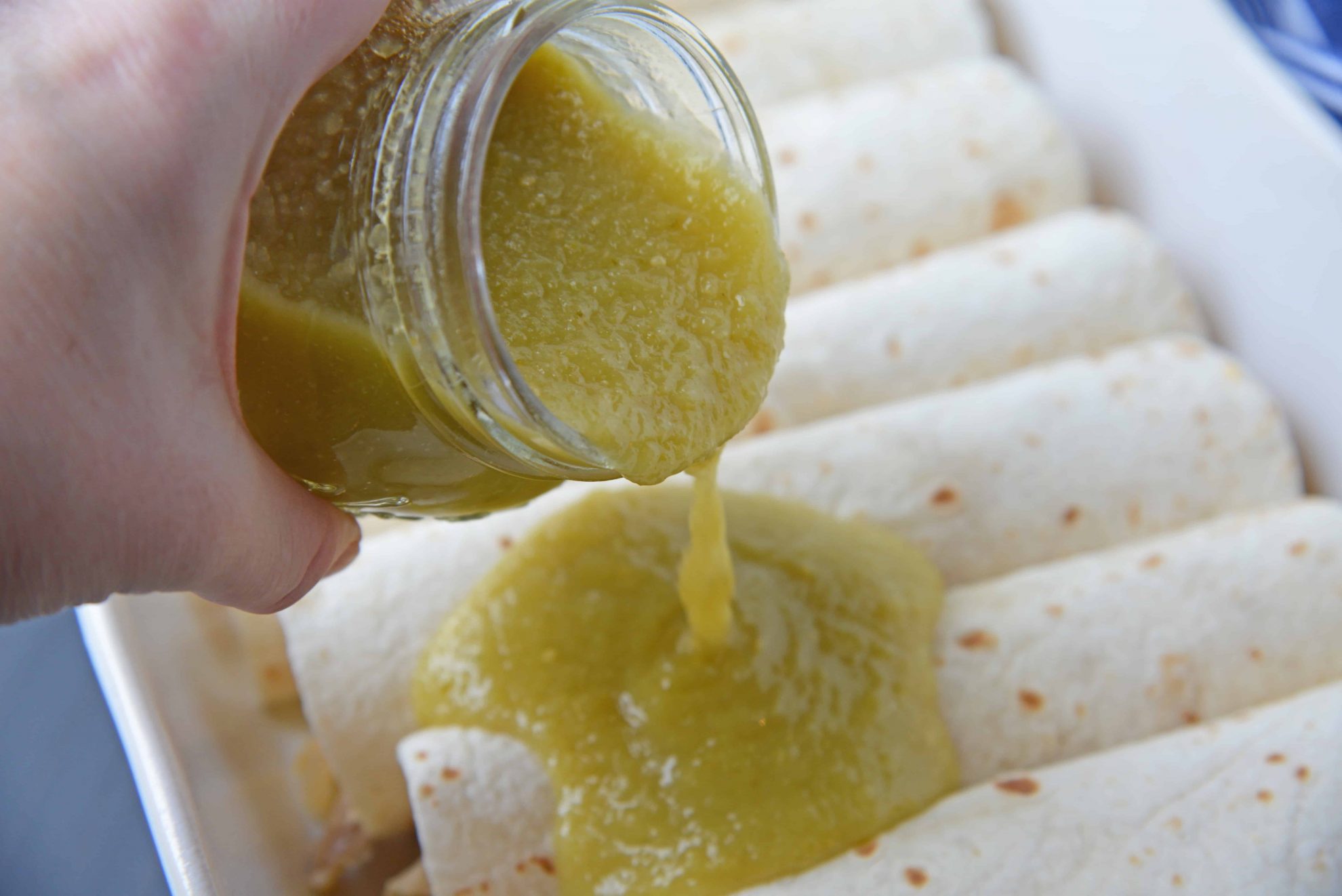 green enchilada sauce pouring over burritos