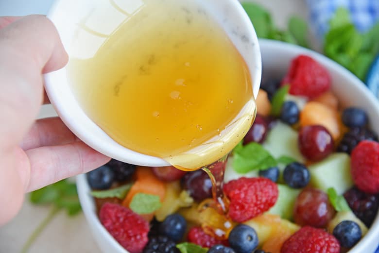 pouring fruit salad dressing over berries 