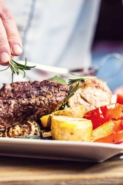 hand garnishing steak with fresh herbs