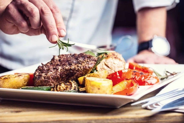 hand garnishing steak with fresh herbs