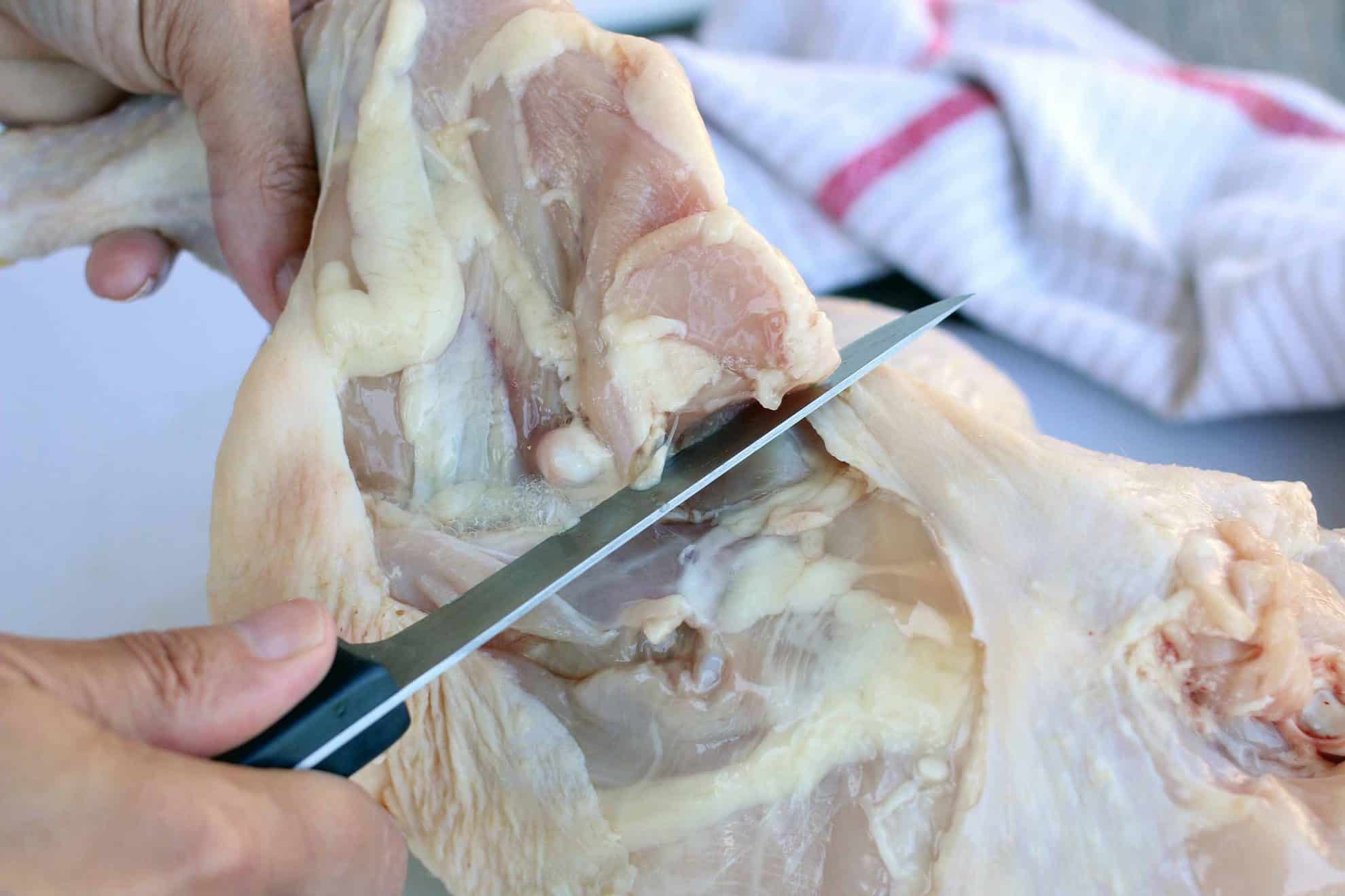 Slicing through the skin to remove the leg quarter from a whole chicken