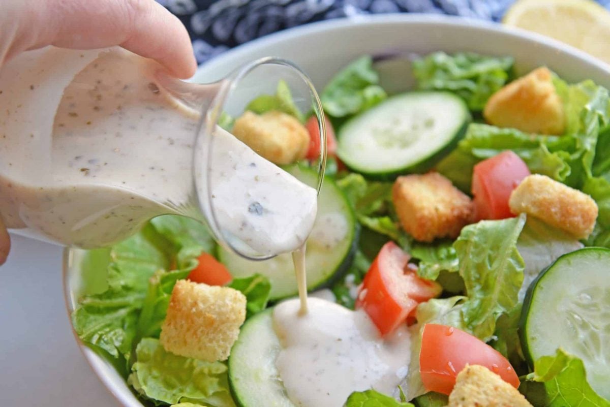 Greek salad dressing pouring over green salad