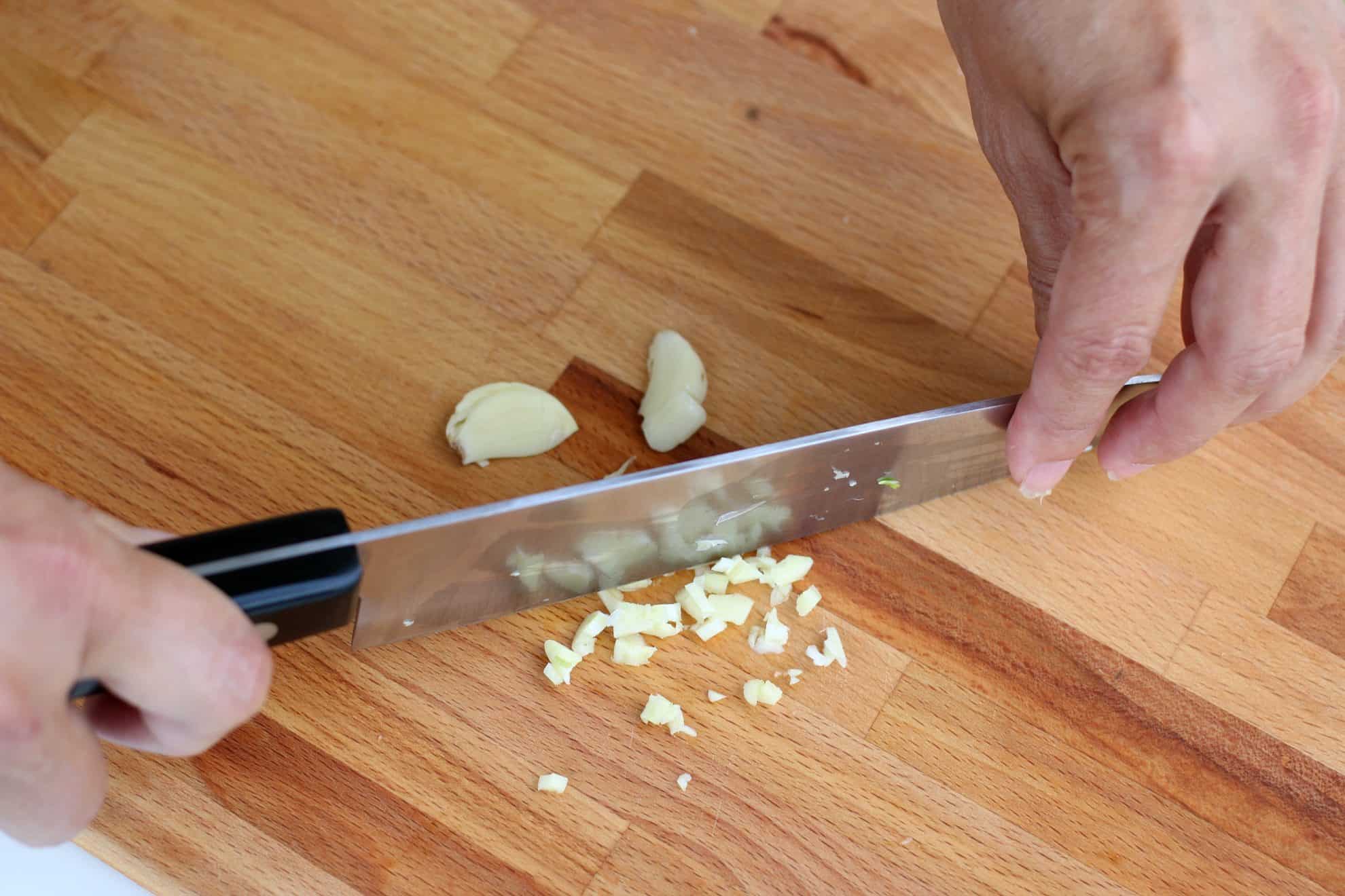 Mincing garlic cloves after they have been smashed with the blade of a knife.