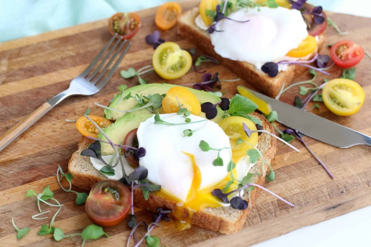Poached egg on avocado toast garnished with micro greens and heirloom tomatoes