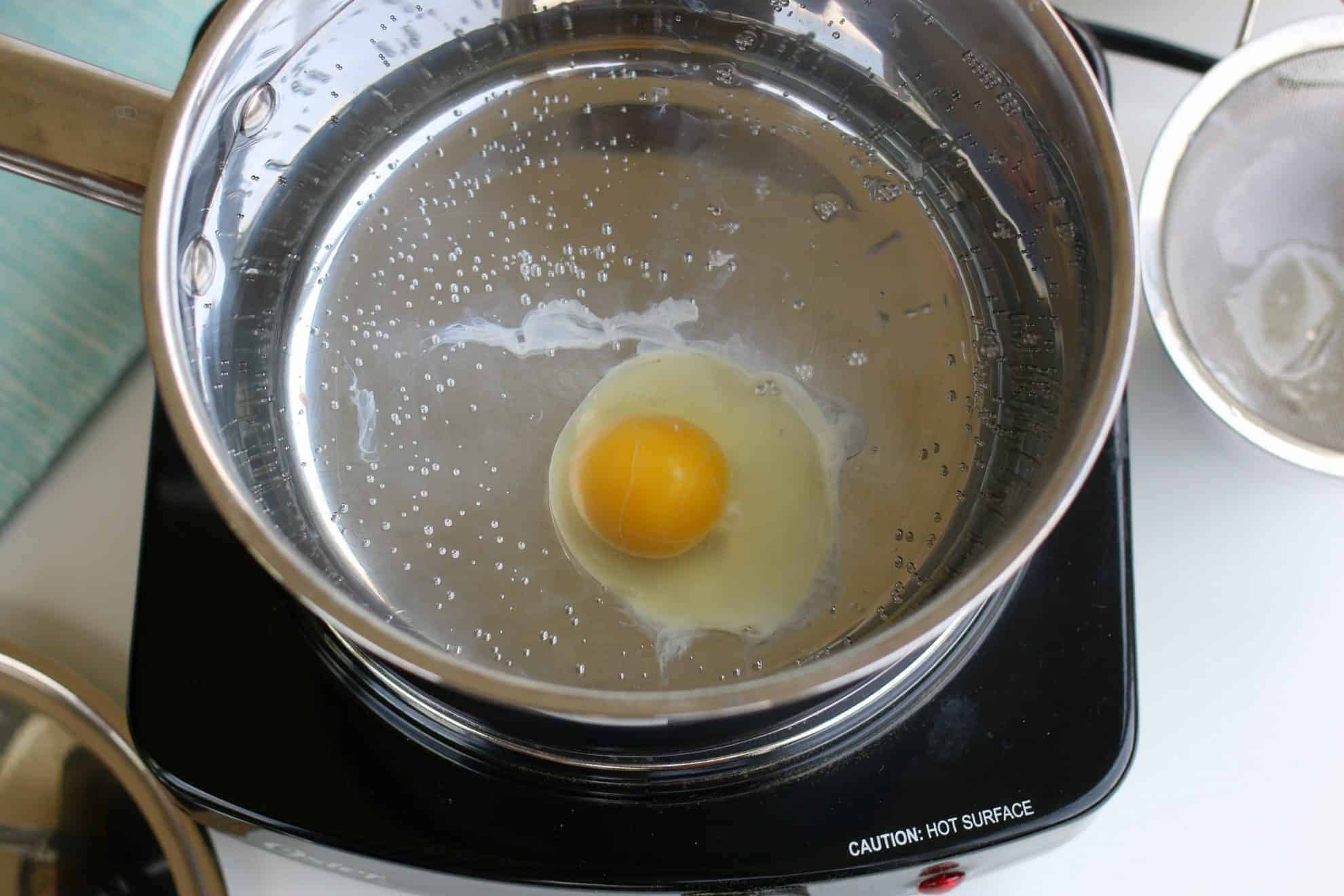 A single egg in a pan of simmering water poaching an egg