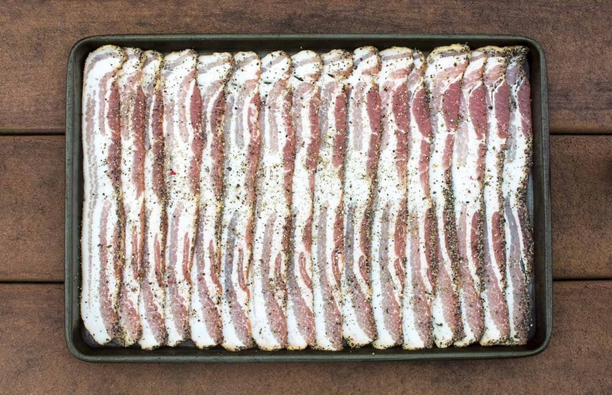 Seasoned uncooked bacon on a baking sheet