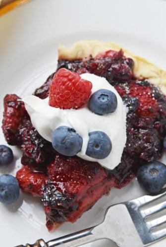 slice of mixed berry pie with whipped cream and cresh berries