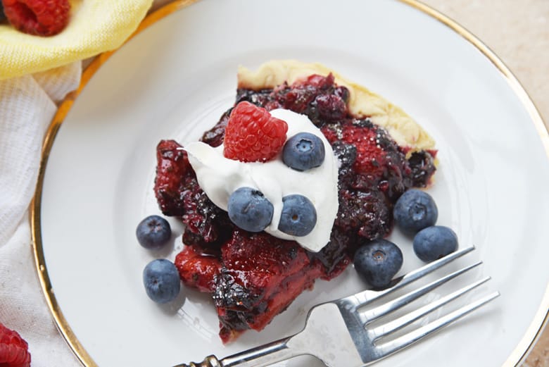 slice of mixed berry pie with whipped cream and cresh berries