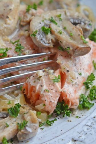 Fork cutting into a salmon fillet in asiago mushroom sauce