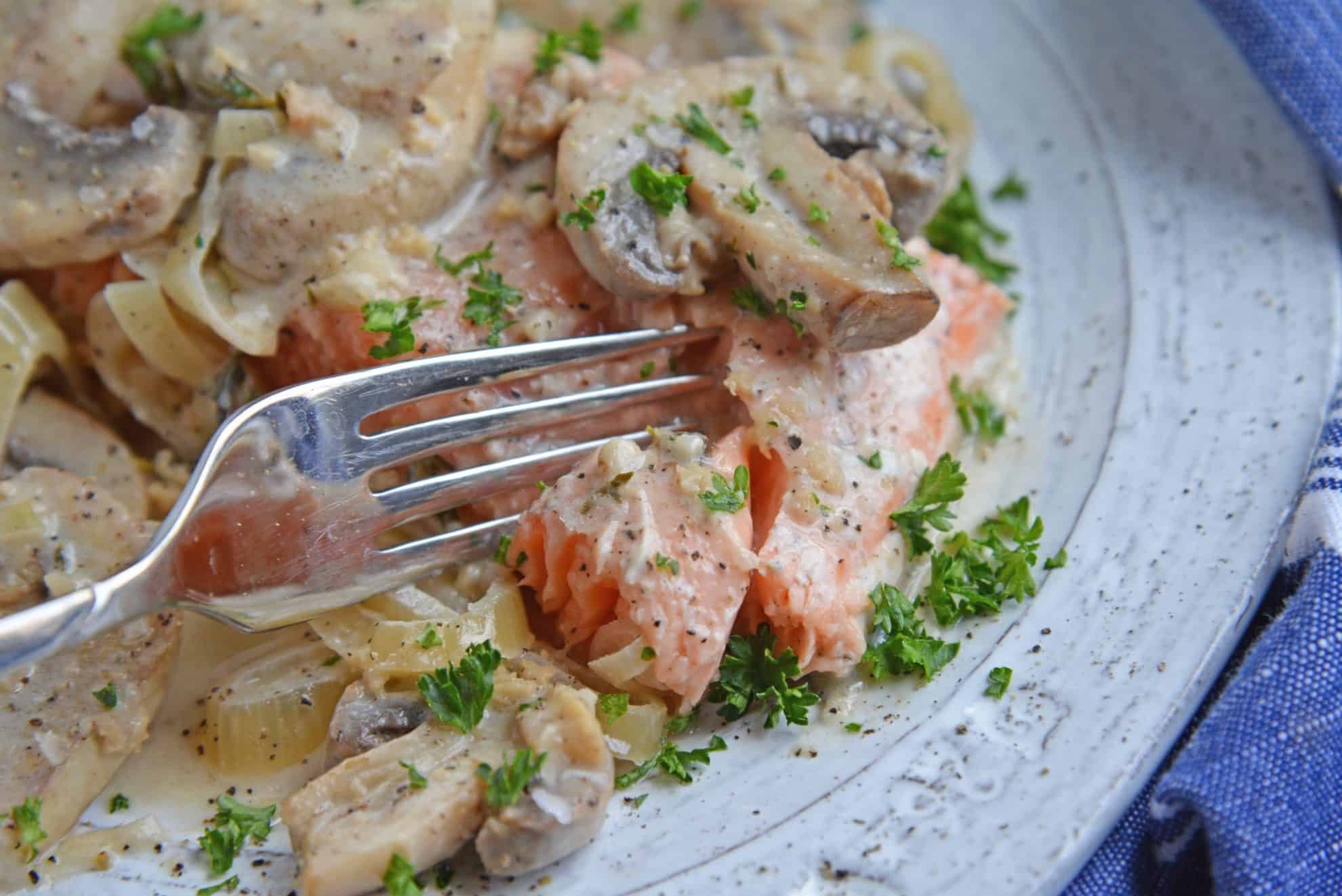 Fork cutting into a salmon fillet in asiago mushroom sauce