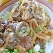 Salisbury steak plated with buttered noodles and peas