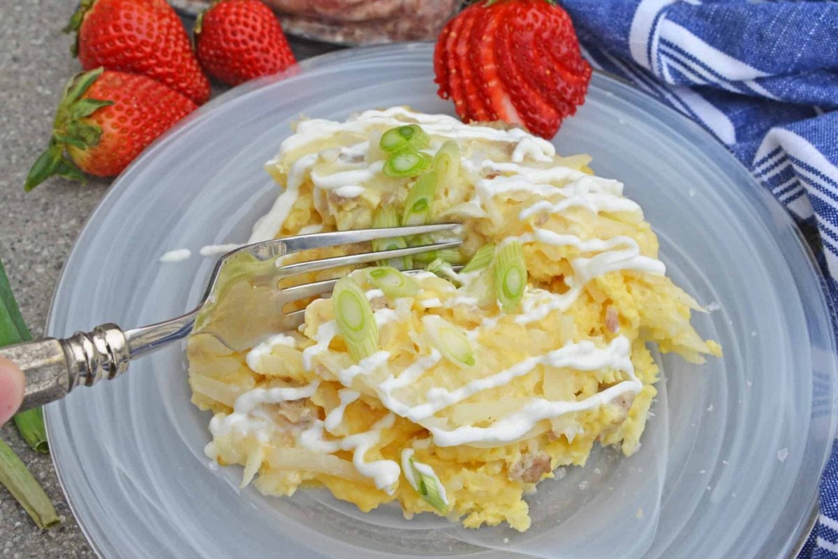 Fork digging into a slice of breakfast casserole with sour cream and green onions 