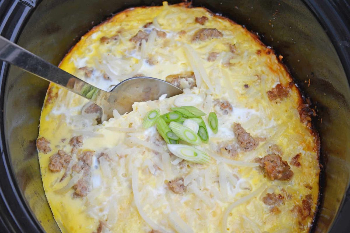 Breakfast casserole being scooped out of a slow cooker bowl 