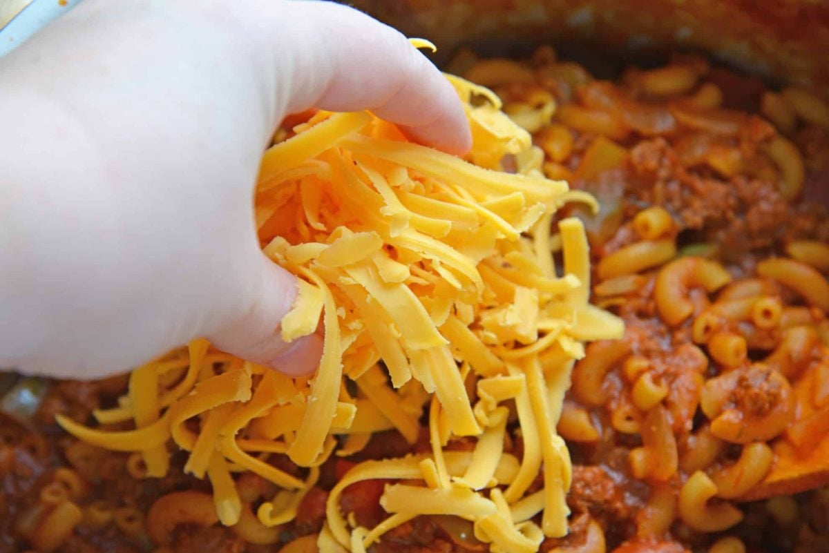 hand adding cheese to beef goulash