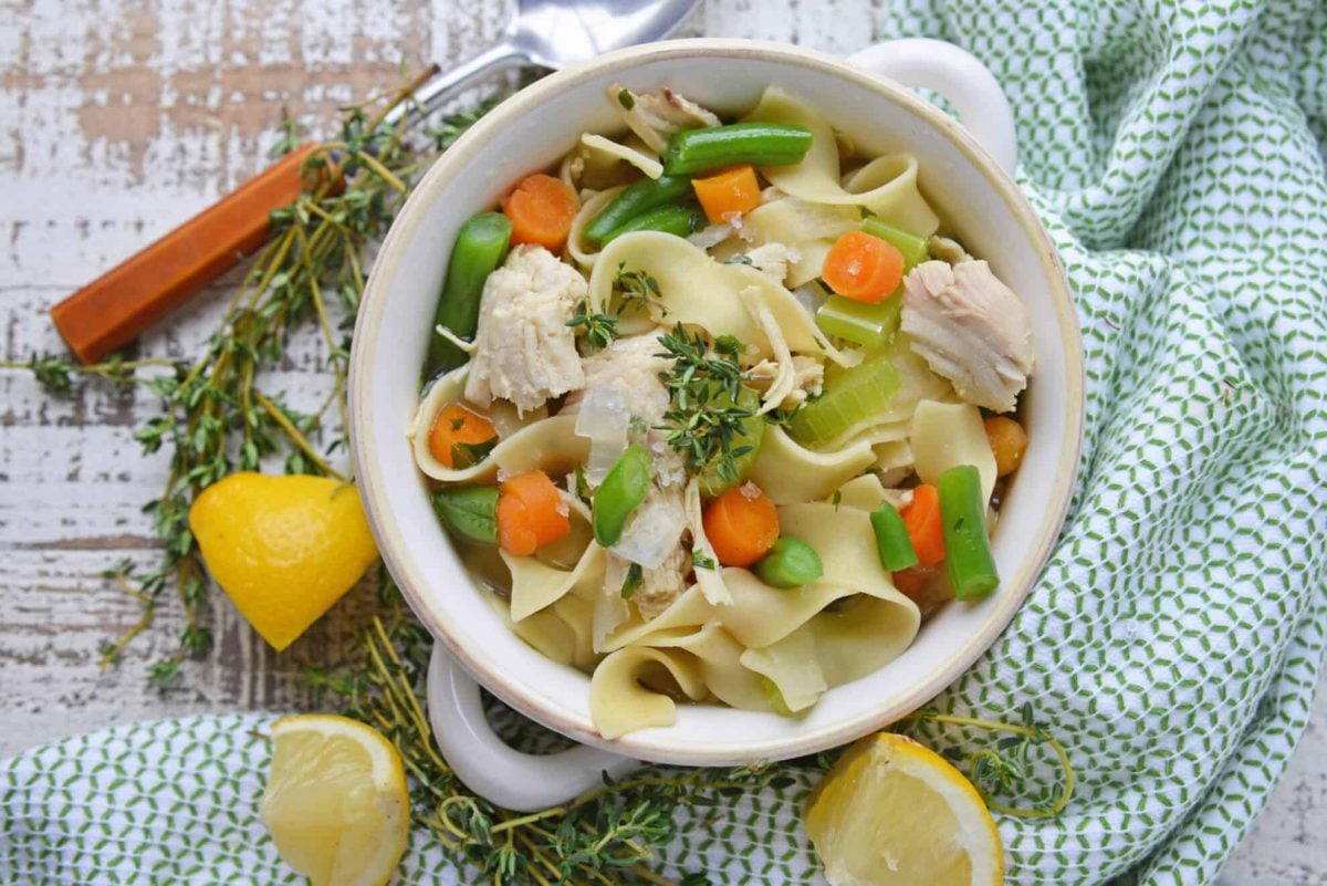 overhead of chicken noodle soup with lemon