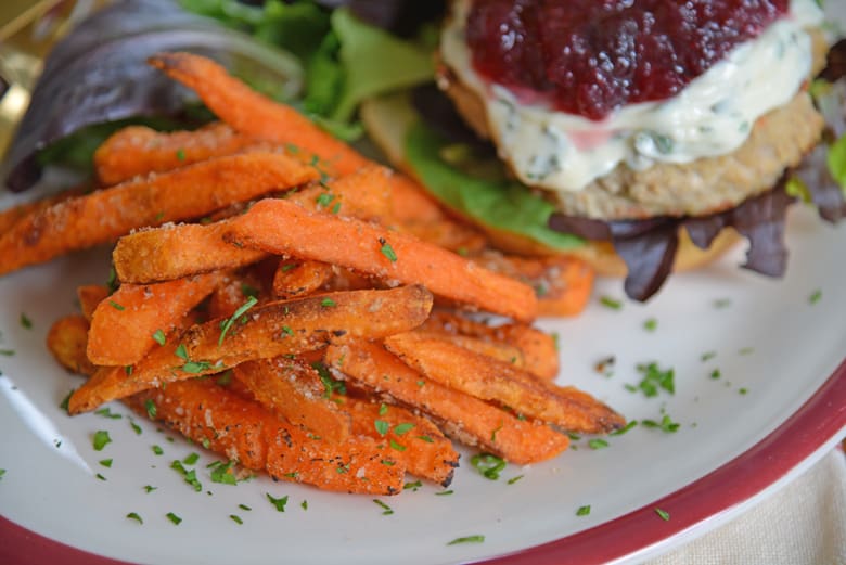 Sweet potato fries on a white dinner plate with salad and a burger 