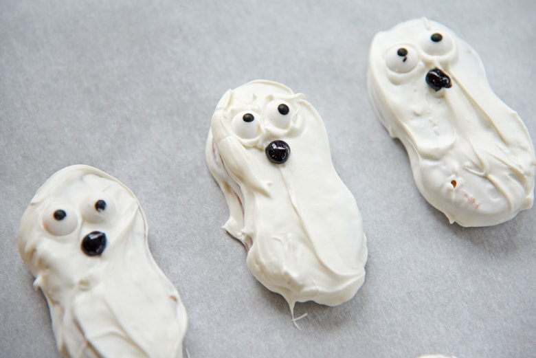 Three ghost cookies lined up on a sheet of parchment paper 