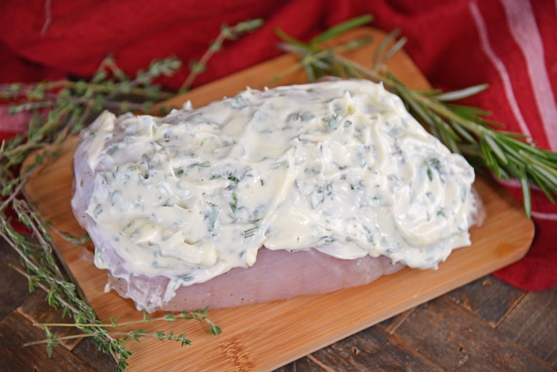Herbed mayo slathered onto turkey breast on a cutting board 