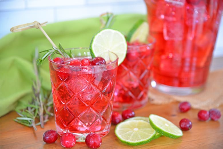 Side view of cocktail glass with cranberries, ice cubes and lime