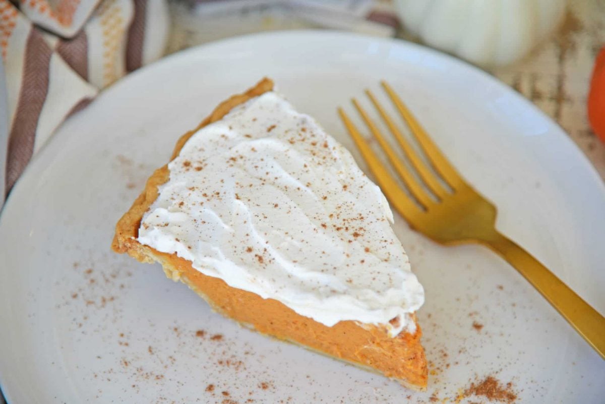 Slice of frosted pumpkin pie on a white plate with gold fork 