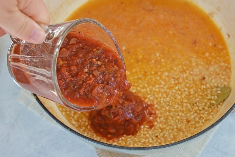 Pouring salsa into a simmering pot of rice and broth 