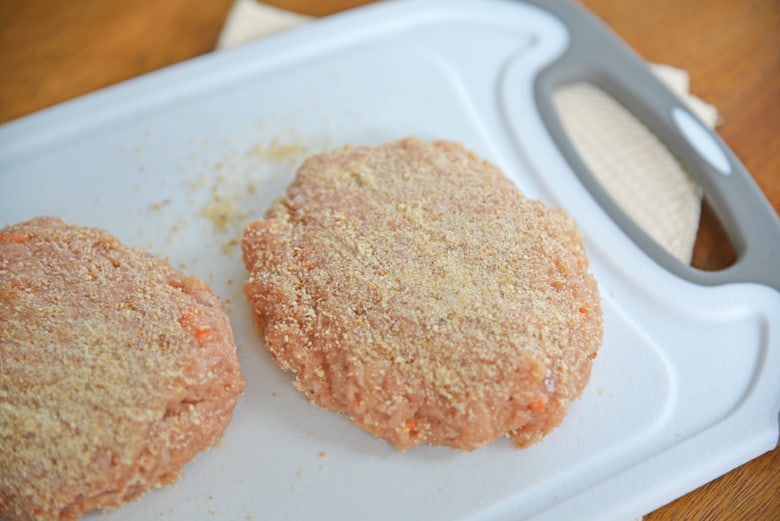 Turkey burger patties with bread crumbs on a cutting board 