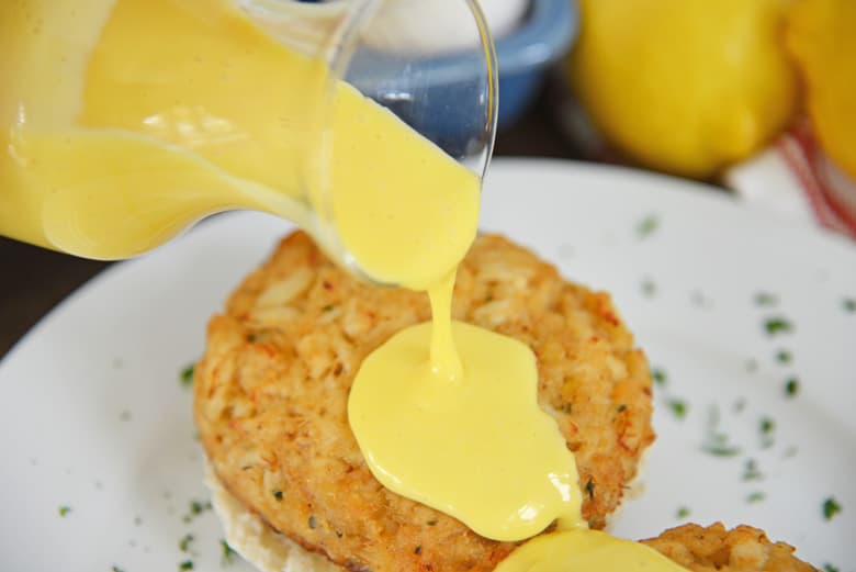 hollandaise sauce pouring over crab cakes 