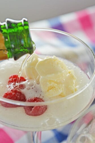 pouring champagne into a glass with ice cream and raspberries
