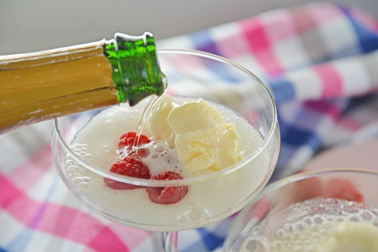 pouring champagne into a glass with ice cream and raspberries