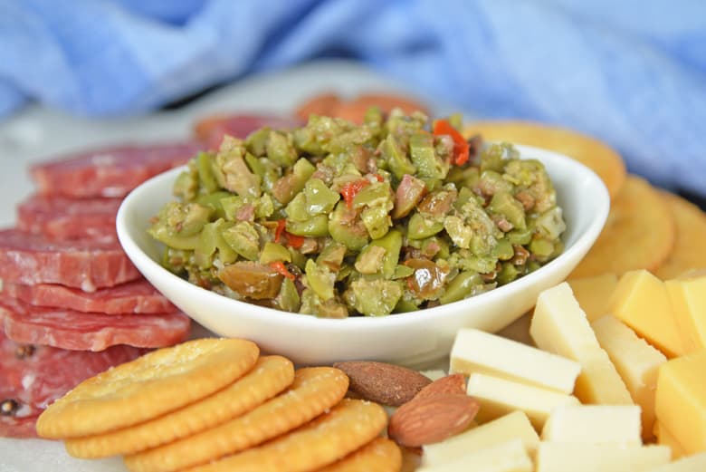 Side angle of olive tapenade surrounded by cheese, crackers and pepperoni 