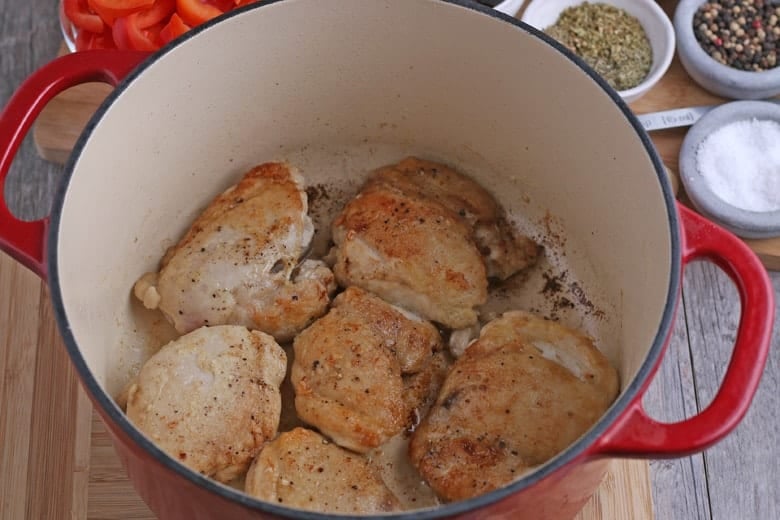 Browned and seasoned chicken thighs in a red Dutch oven 