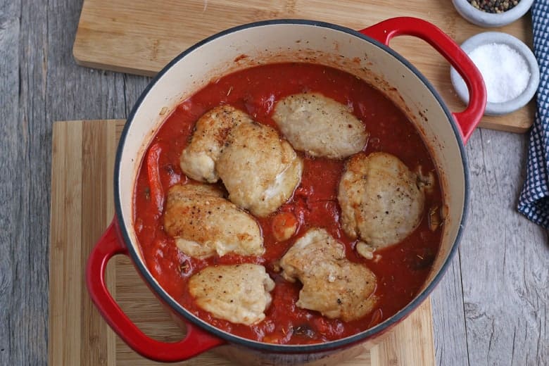 Chicken thighs simmering in a red tomato sauce for chicken cacciatore 