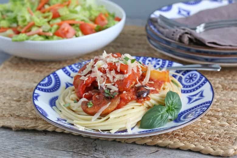 Chicken cacciatore over spaghetti on a blue and white plate. 