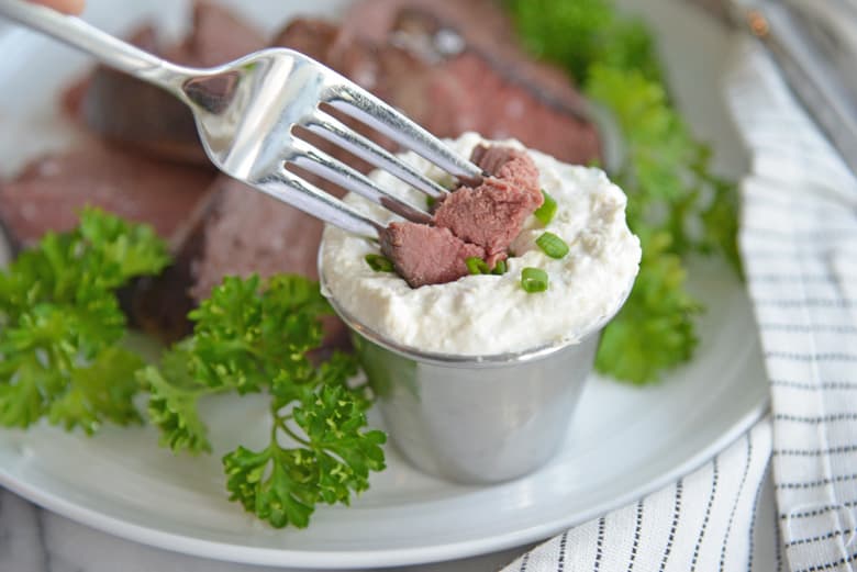 piece of beef dipping in to a ramekin of horseradish sauce 