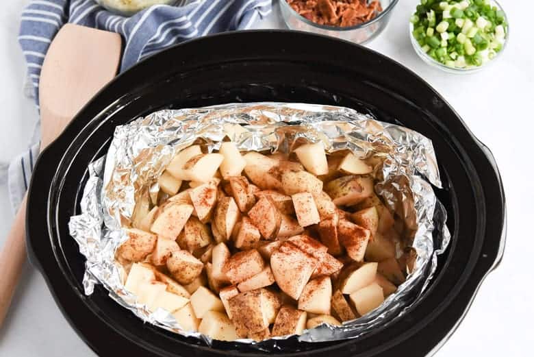 Raw potatoes in slow cooker with seasoning 