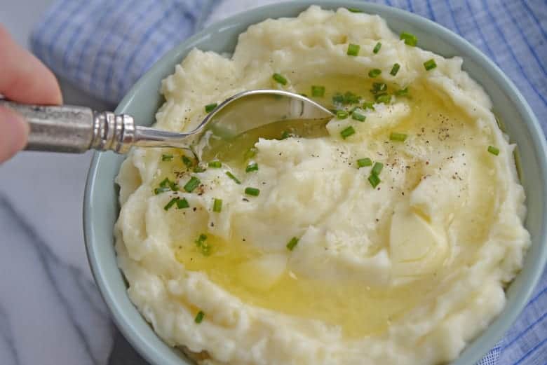 Spoon dipping into creamy mashed potatoes with melted butter 
