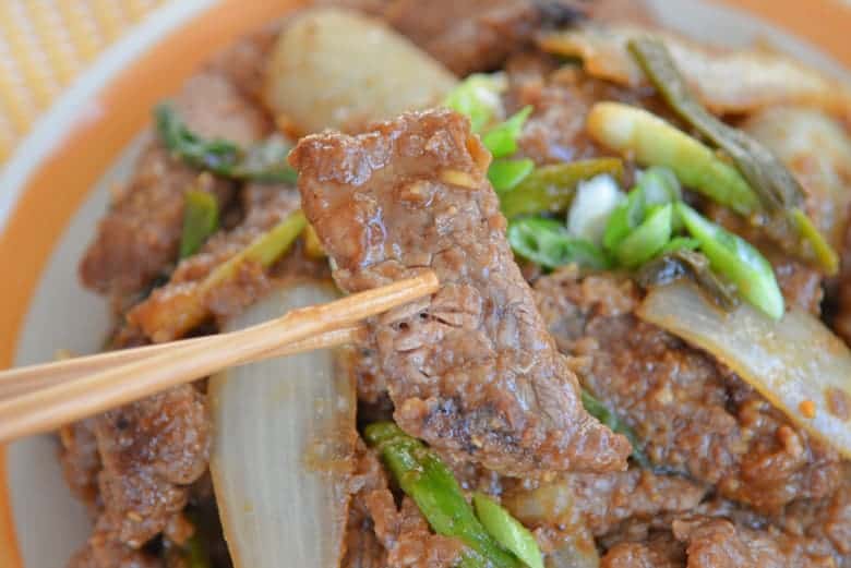 Chopsticks holding a piece of Mongolian beef 