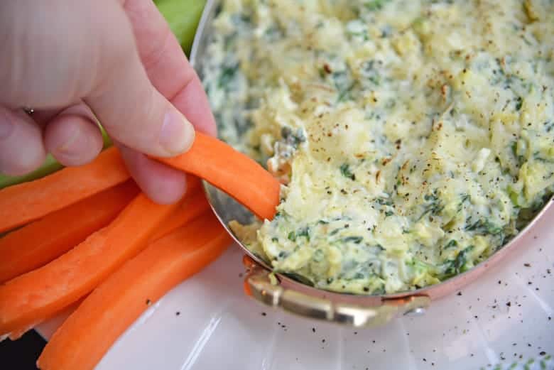 Carrot dipping into best spinach artichoke dip 