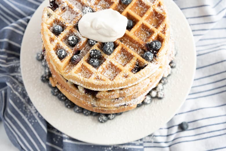 Stack of blueberry waffles with powdered sugar, blueberries and whipped cream 