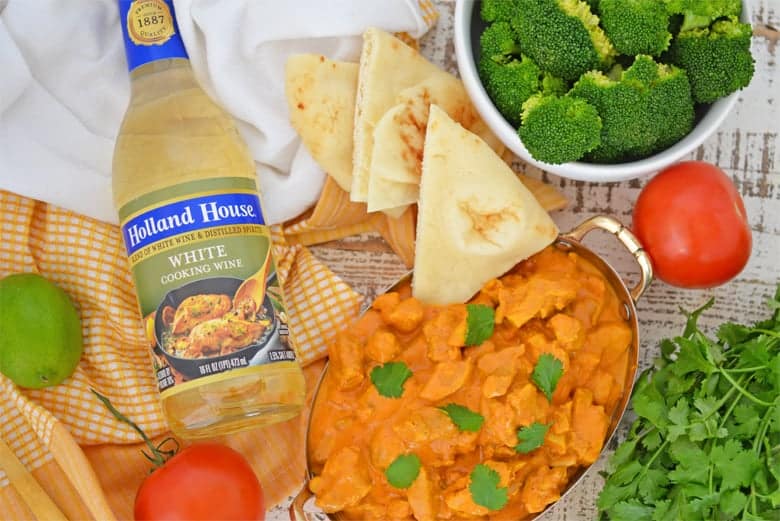 Butter chicken in a copper serving dish with fresh ingredients 