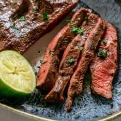 angled shot of sliced flank steak on blue plate with lime