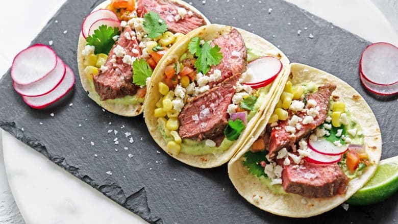 Serving platter of flank steak tacos with radish slices 